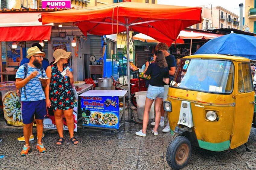 Un carrito de comida callejera con un vehículo amarillo, gente comiendo y un puesto de tacos. 4