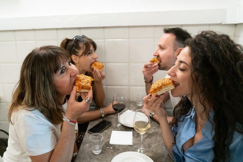 Vier personen zitten aan tafel, pizza eten en wijn drinken. 2