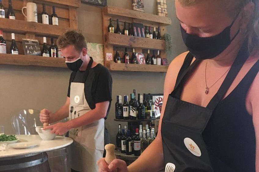 Zwei Personen in einer Küche, eine bereitet Essen zu, während die andere einen Holzstößel hält. 2