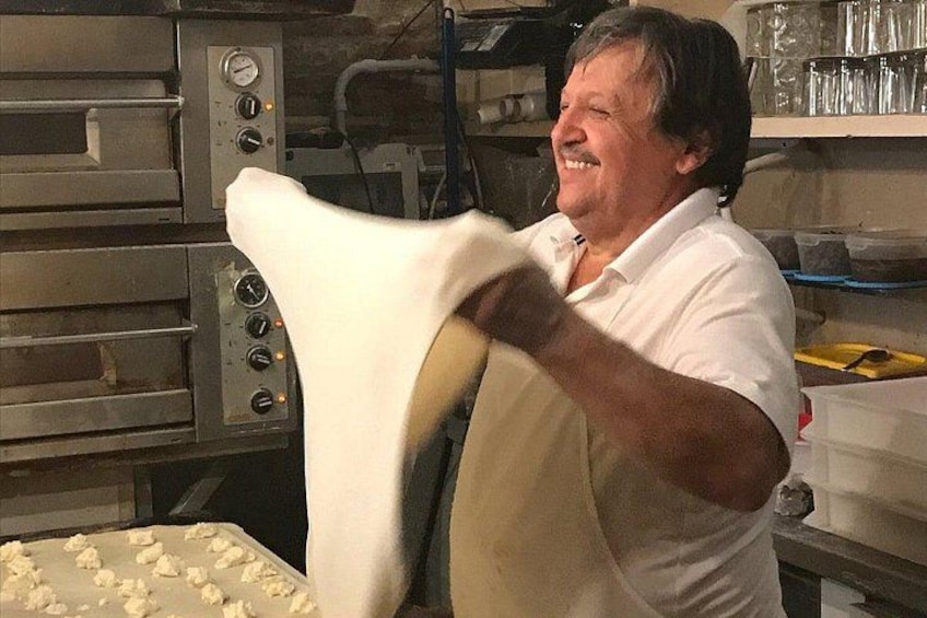 A person in a white shirt working with dough on a large rolling pin in a kitchen with industrial ovens. 2