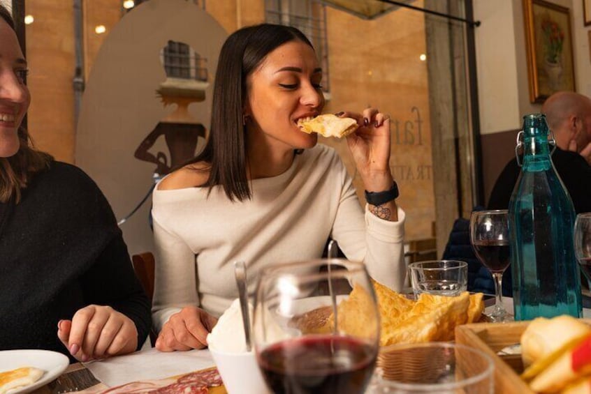 A person eating a piece of bread at a table with a glass of red wine and a bottle of water. 5