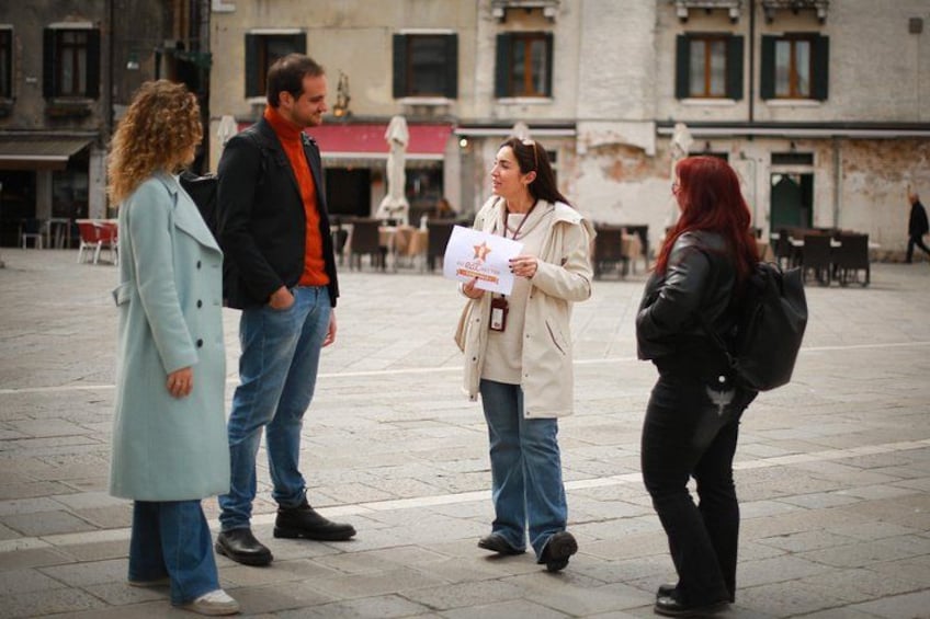 Un grupo de personas de pie en una plaza pública con edificios al fondo. 2