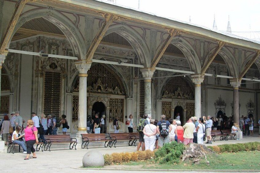 Un edificio histórico con arquitectura ornamentada, gente sentada en bancos y una zona verde frente a él. 4