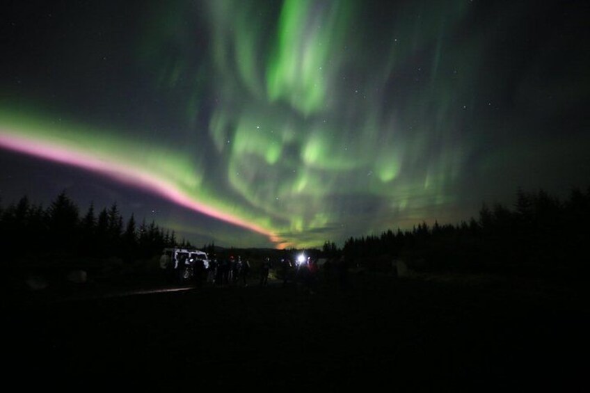 Auroras boreales sobre un paisaje boscoso con una carretera y vehículos. 3