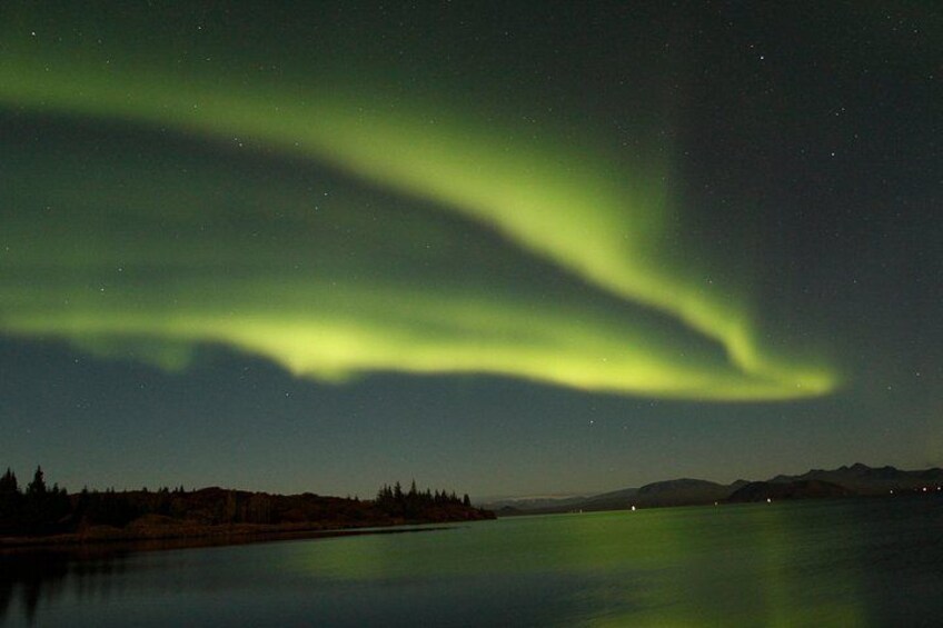 Cielo nocturno con la aurora boreal sobre un lago tranquilo y montañas a lo lejos. 5