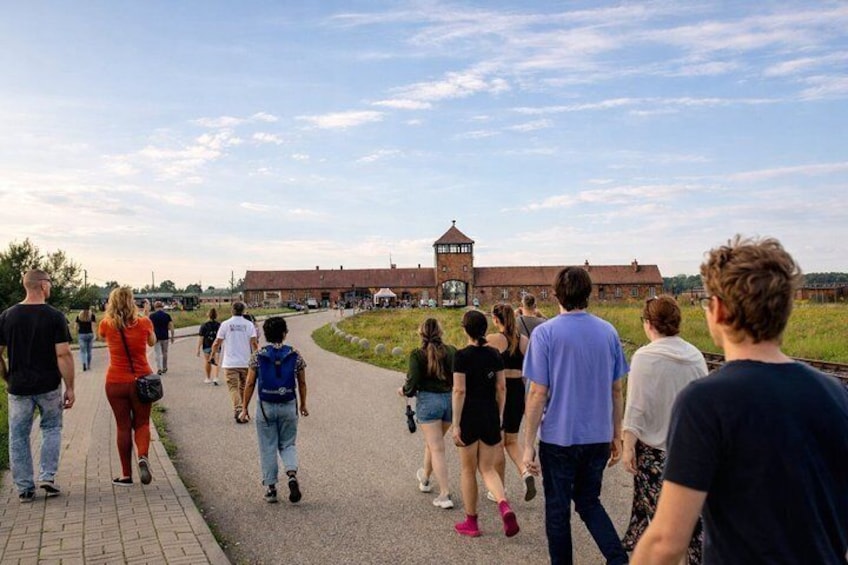 A group of people walking on a paved path towards a large brick building with a tower. 1