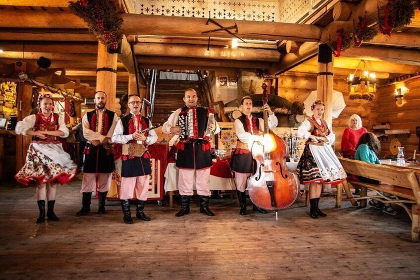 A group of people in traditional Bavarian attire performing music in a rustic wooden room. 1