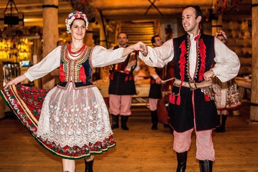 A couple in traditional attire dancing in a rustic setting with wooden beams and tables. 4