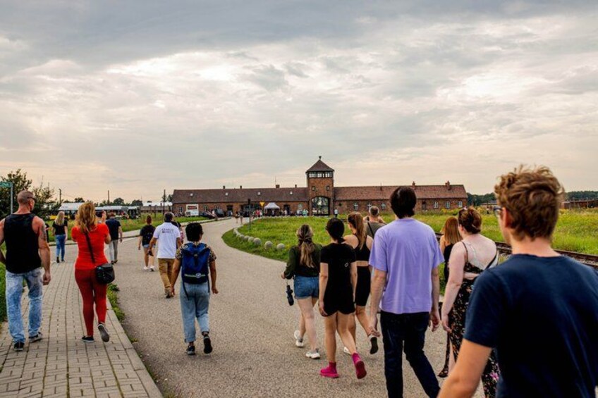 A group of people walking on a paved path towards a large brick building with a tower. 4