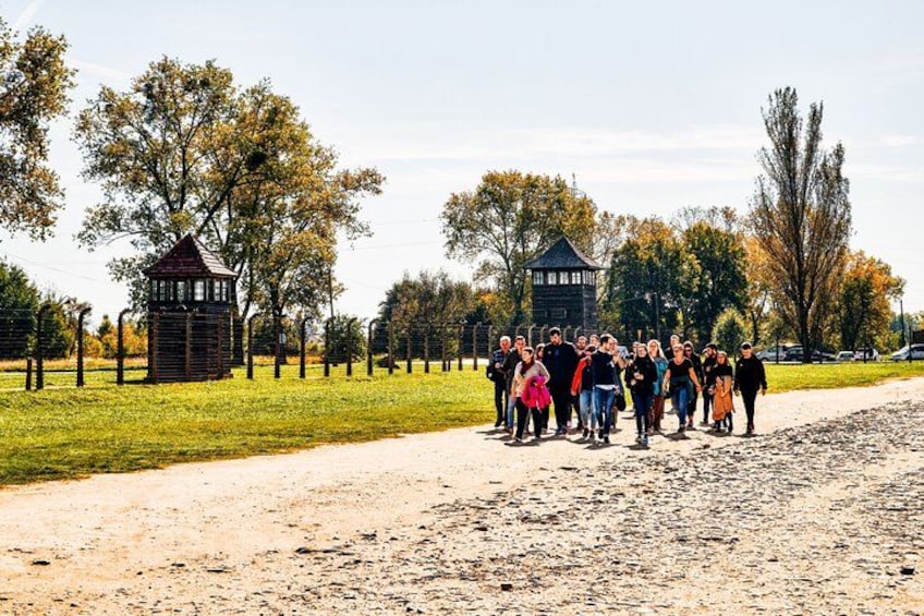 A group of people standing on a dirt path in a park with two wooden structures and trees in the background. 3
