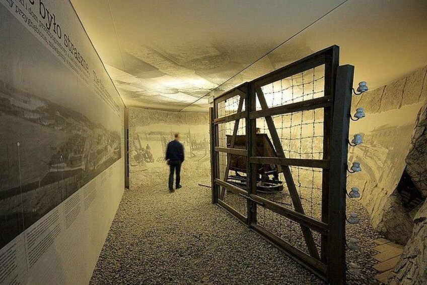 Een persoon loopt door een tunnel met een metalen poort en een poster op de muur. 2