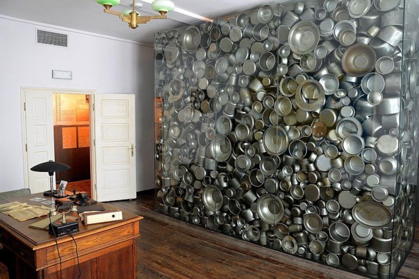 A room with a wall covered in metal cans, a wooden desk with a lamp, and a door leading to another room. 2