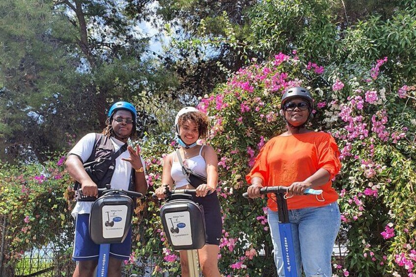 Three people on scooters with helmets, surrounded by pink flowers and trees. 3
