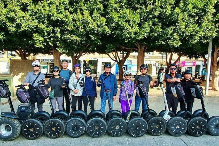 Een groep mensen met Segways staan op rij op een trottoir. 2
