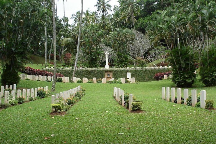 Un cementerio con lápidas blancas alineadas en filas, rodeado de exuberante follaje y palmeras. 1