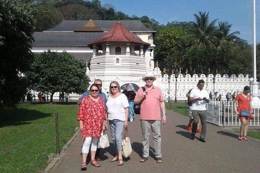 A group of people standing in front of a white building with a red roof, surrounded by greenery and a white fence. 2