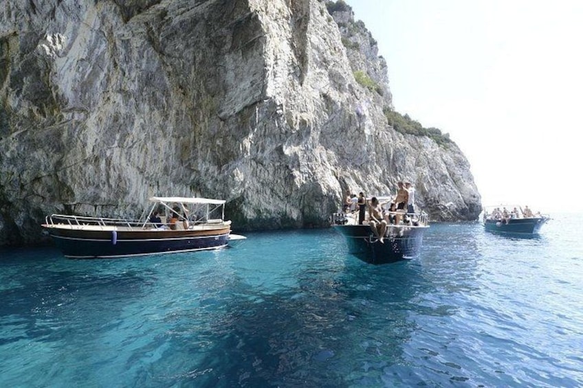 Three boats on clear blue water near rocky cliffs. 1
