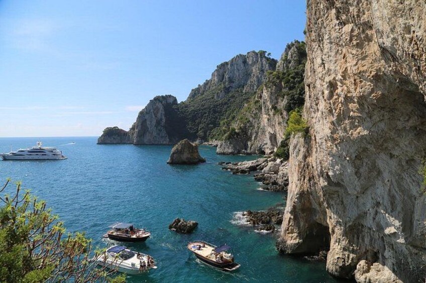 A coastal scene with boats, rocky cliffs, and clear blue water. 5