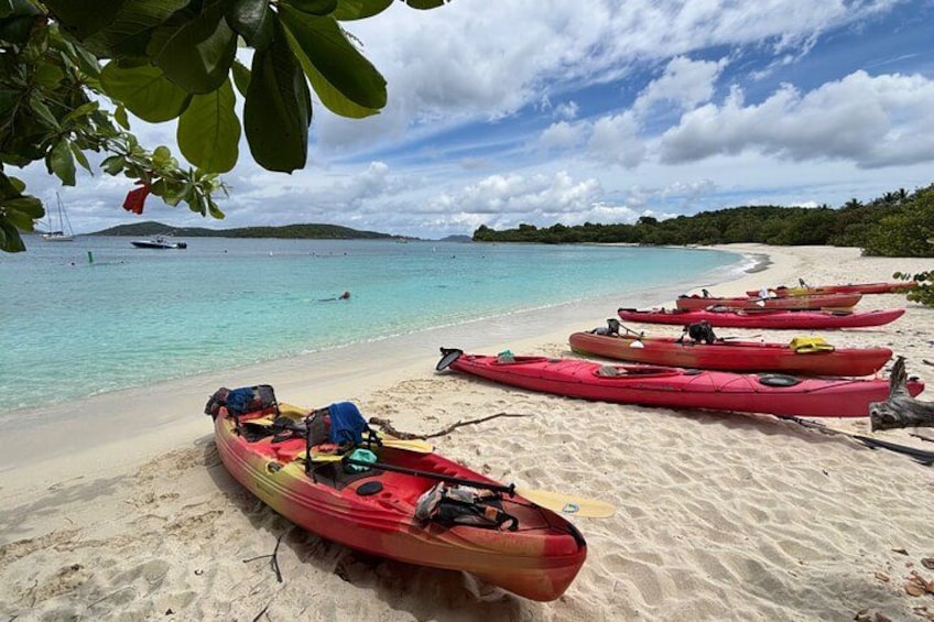 Une plage où l’on voit des kayaks alignés sur le sable et un bateau sur l’eau. 2