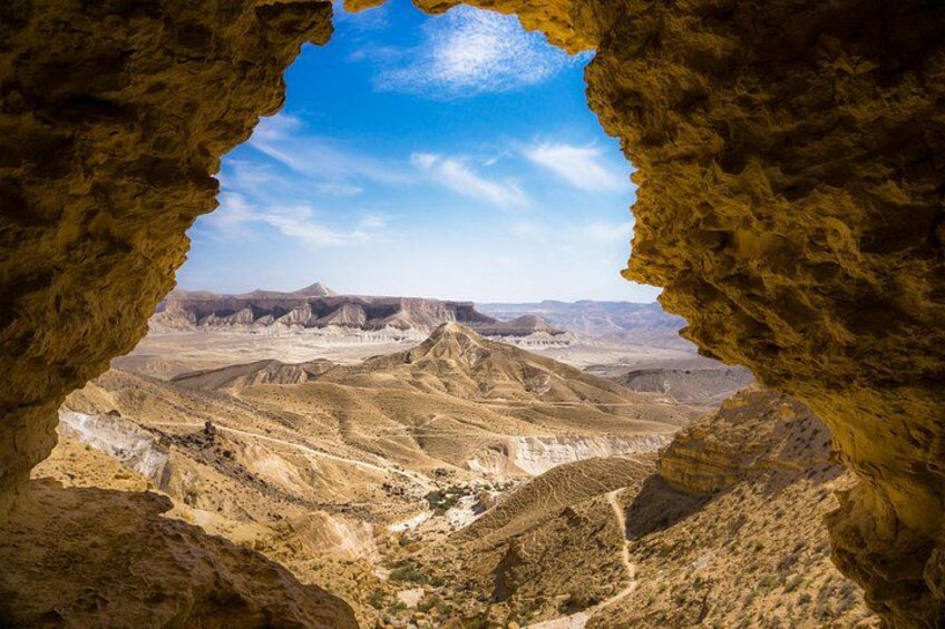 A rocky landscape with a cave opening, revealing a vast desert valley and distant mountains. 3