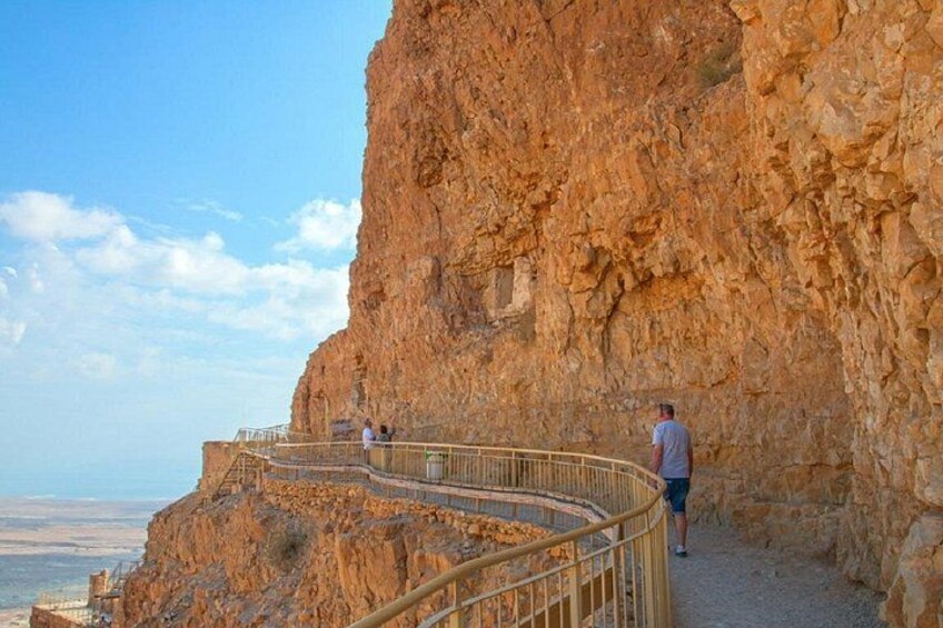A rocky cliff with a metal railing and a person standing on it. 1
