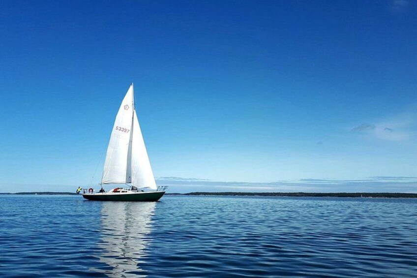 Ein Segelboot mit weißer Segel auf ruhigem Wasser unter klarem Himmel. 2