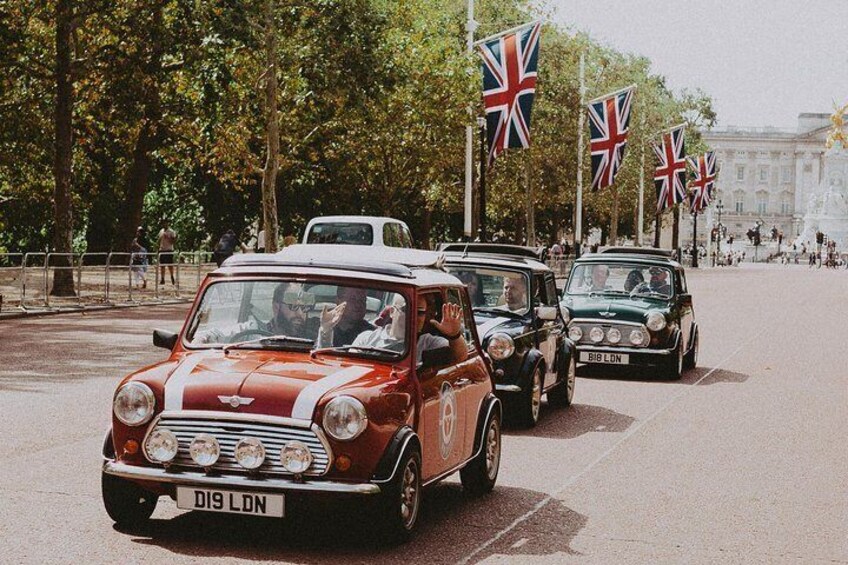 Vintage cars lined up on a street with British flags and a crowd of people in the background. 1
