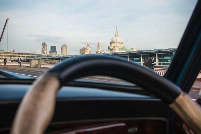 A steering wheel, dashboard, and a cityscape with a prominent dome and skyscrapers in the background. 3