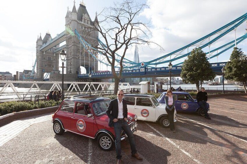 A red convertible car parked in a parking lot with a bridge and tower in the background. 5