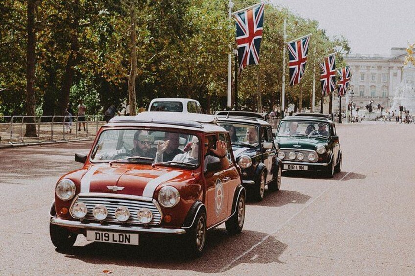 Vintage cars on a city street with flags and a fountain in the background. 2