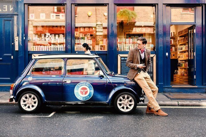 A vintage car parked on a street with a person sitting on the hood. 3
