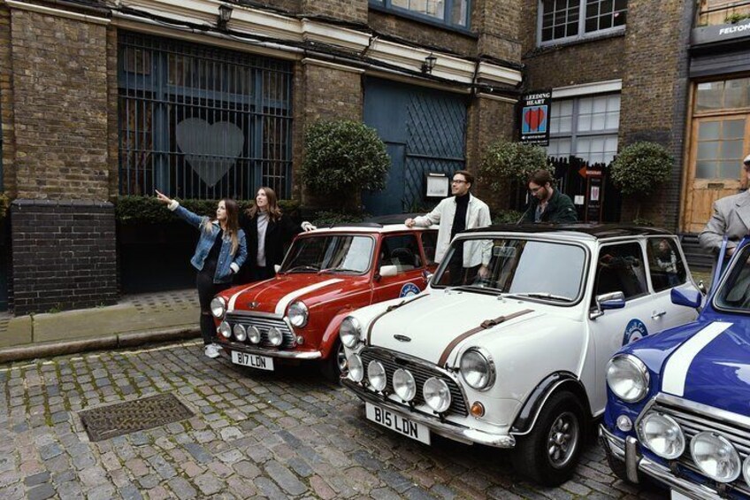 Vintage cars parked on a cobblestone street in front of a brick building with a heart-shaped window. 4