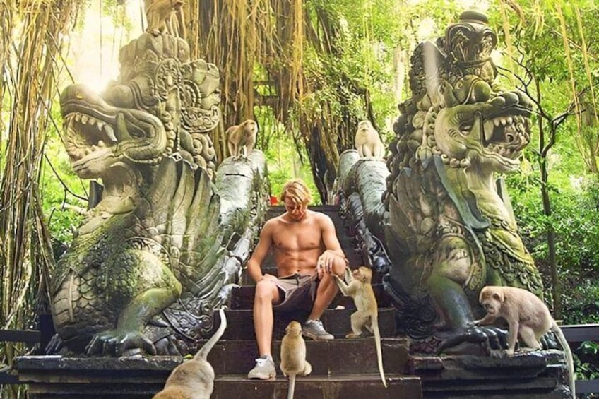 A person sitting on a stone bench surrounded by large stone sculptures of mythical creatures in a lush, green forest. 1