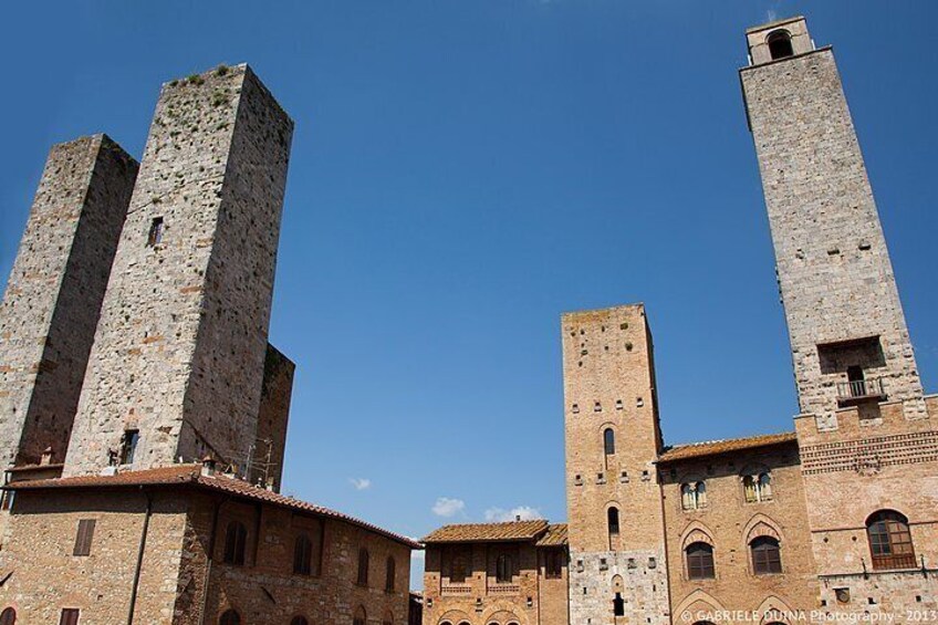 Ein historisches Steinhaus mit zwei hohen Türmen und einem kleineren Gebäude mit Rundbogenfenstern. 2