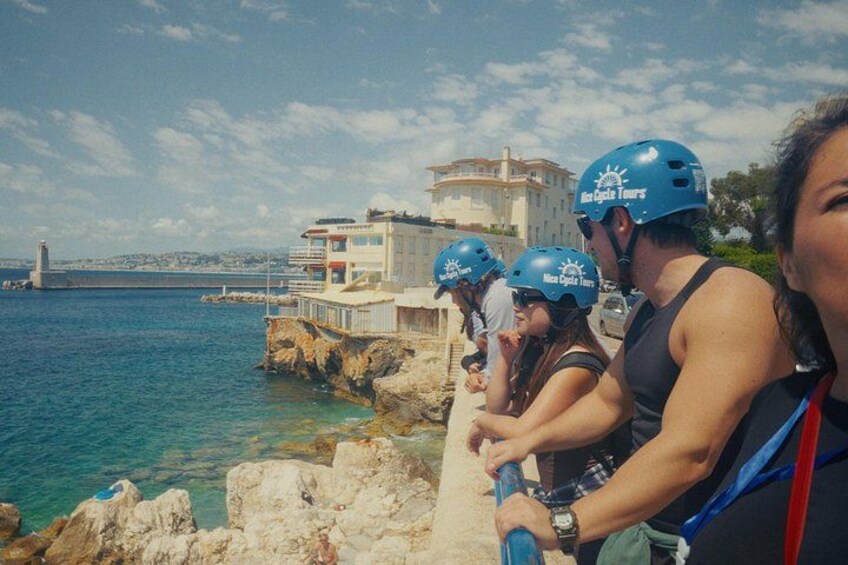 Una zona costiera con persone che indossano caschi, un edificio e un faro sullo sfondo. 5