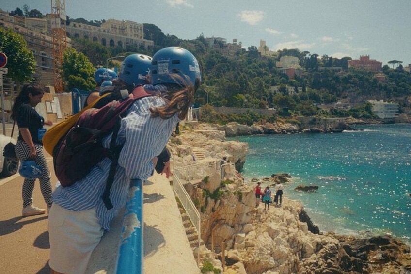 Una zona costiera con scogliere rocciose, mare cristallino e una città sullo sfondo. 3