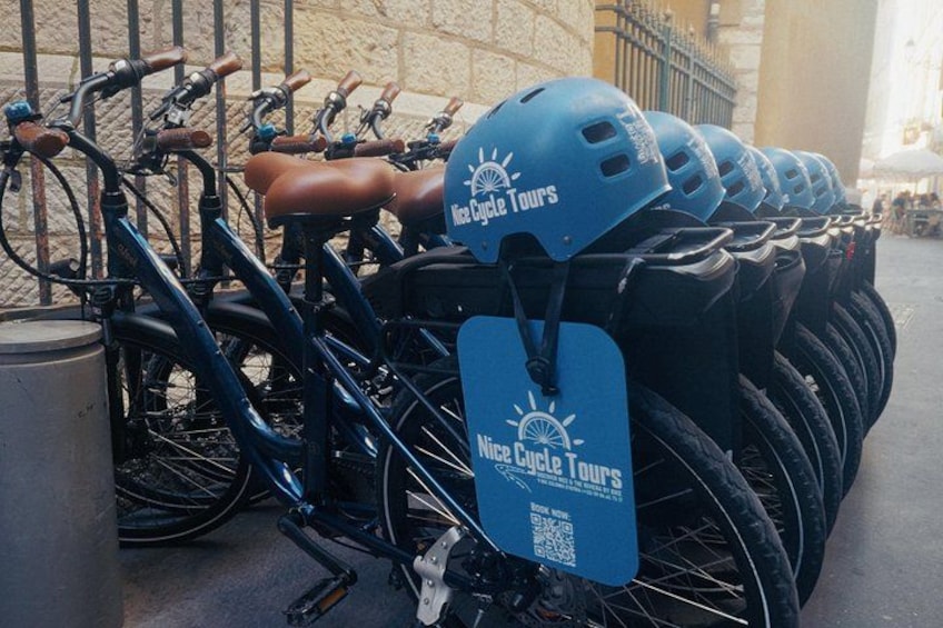 Una fila di biciclette con caschi e un cartello blu che riporta la scritta 'Nice Cycle Tours'. 2