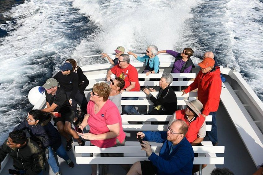 Eine Gruppe von Menschen auf einem Boot mit weißen Geländern, einige tragen Rettungswesten, und das Boot fährt durch das Wasser. 2
