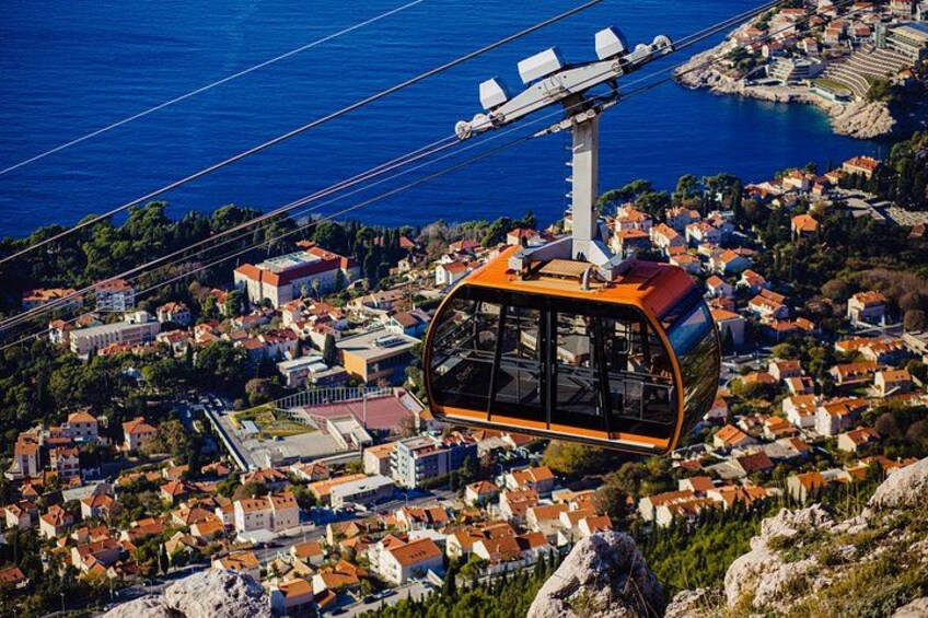 A cable car over a coastal town with buildings and a clear blue sea. 5