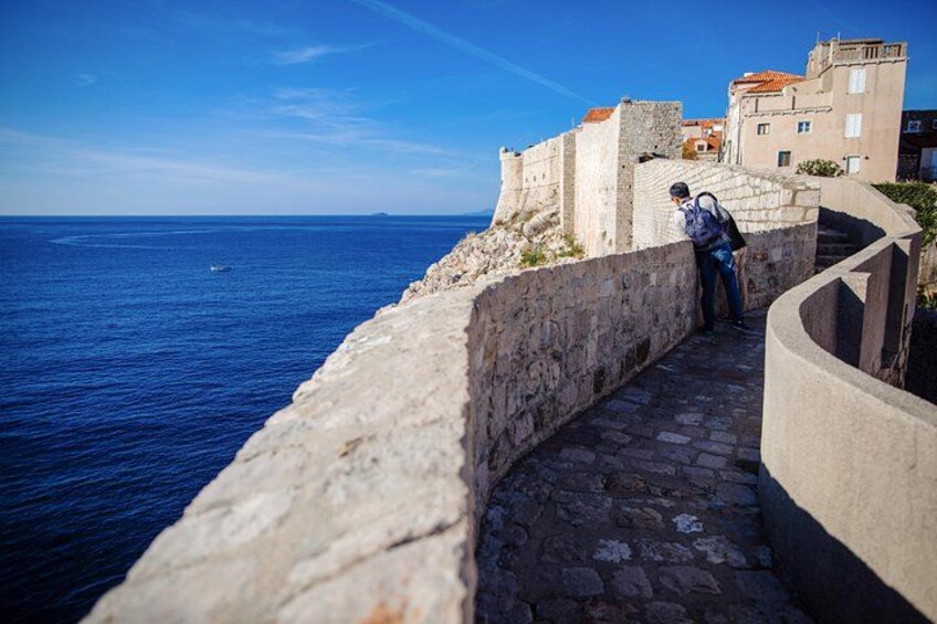 A stone pathway along a coastal wall with a person standing at the end. 4