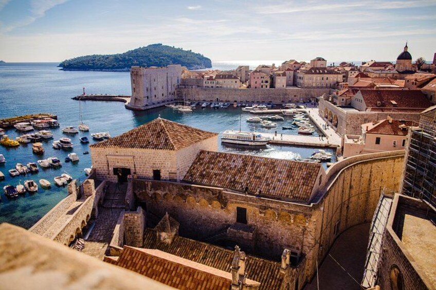 Un paisaje urbano costero con edificios históricos, una estructura fortificada y un puerto con barcos. 2