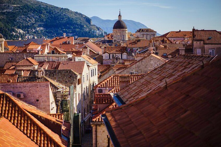 A cityscape with terracotta-roofed buildings, a prominent dome, and a mountainous backdrop. 3
