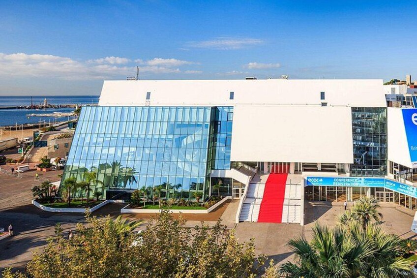 A modern building with a glass facade, a red and white entrance, and a blue sign indicating a conference. 3