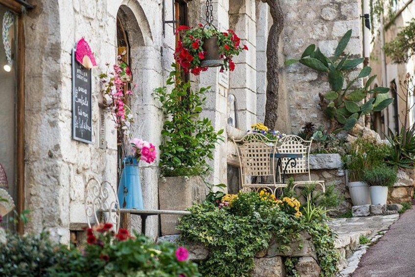 A stone building with a chalkboard sign, a wooden bench, and potted plants. 1