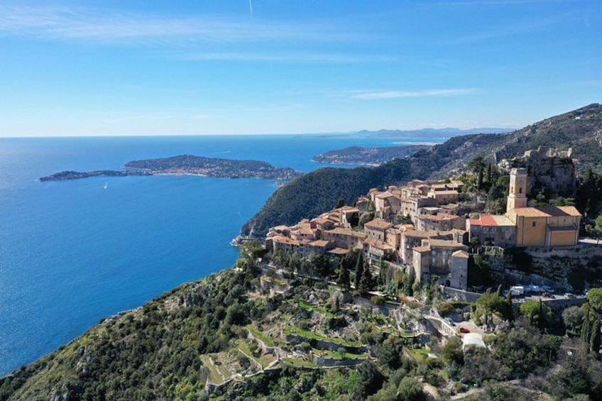 Un borgo costiero con case a terrazze, una chiesa imponente e una vista limpida sul mare e isole sullo sfondo. 1