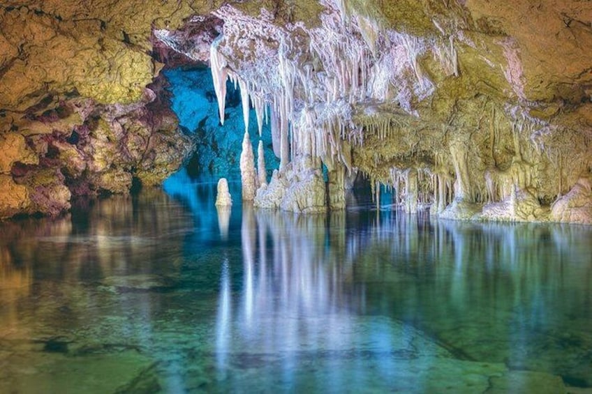 A cave with stalactites and stalagmites, clear water, and colorful rock formations. 4