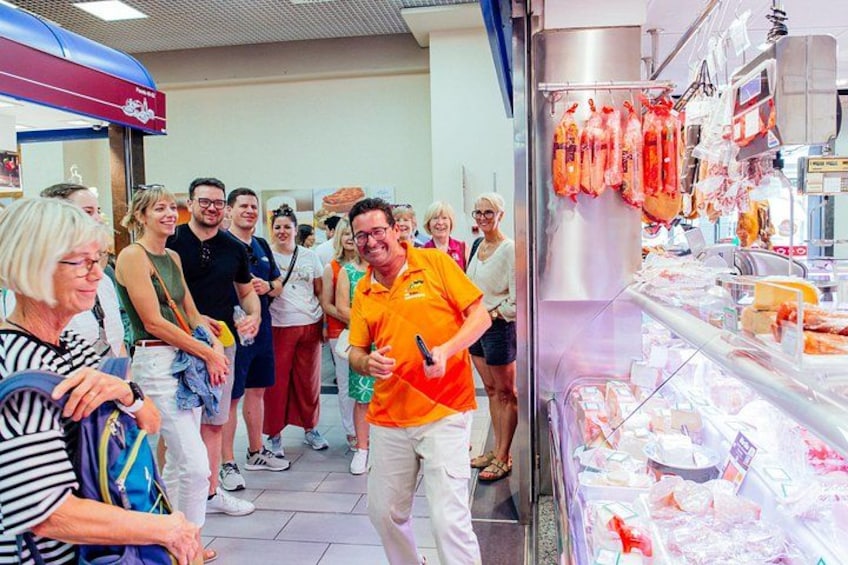 A group of people in a food market, with a man in an orange shirt standing in the foreground. 5