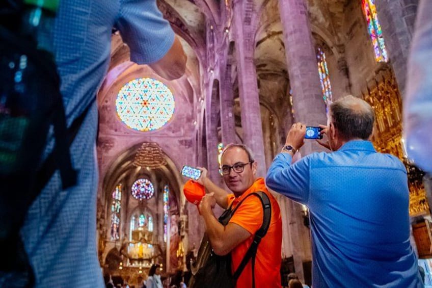 A person in an orange vest taking a photo inside a cathedral with stained glass windows and a large circular window. 2