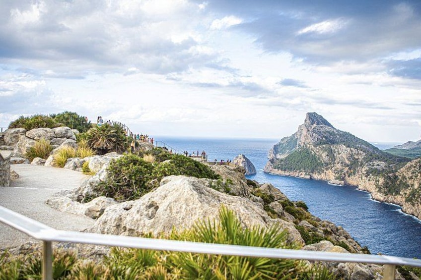 A coastal landscape with rocky terrain, a paved path, and a viewpoint overlooking the sea. 3