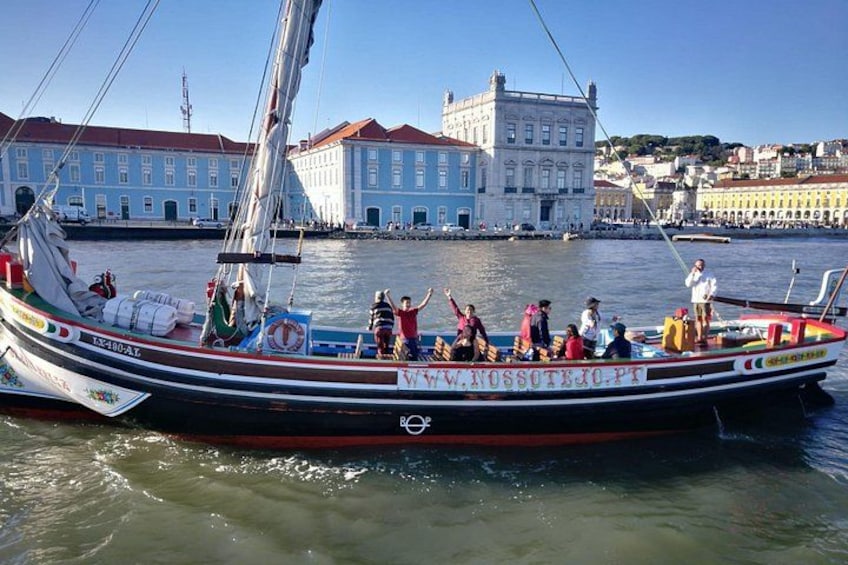 A sailboat with people on board, docked near a waterfront with buildings in the background. 5